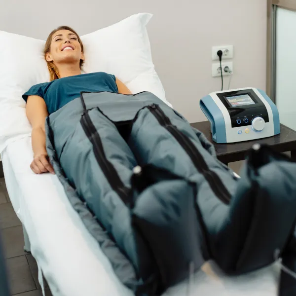 Une femme allongée sur un lit avec un masseur pour les pieds, pratiquant la pressothérapie.